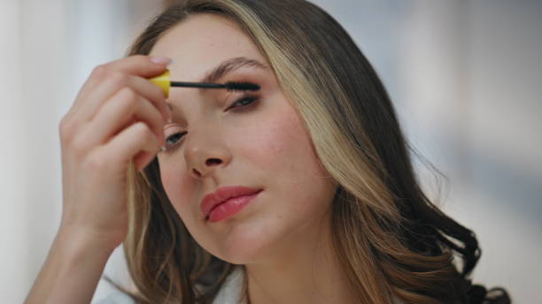 istock Closeup woman holding mascara brushing eyelashes. Smiling woman doing makeup 2178107821