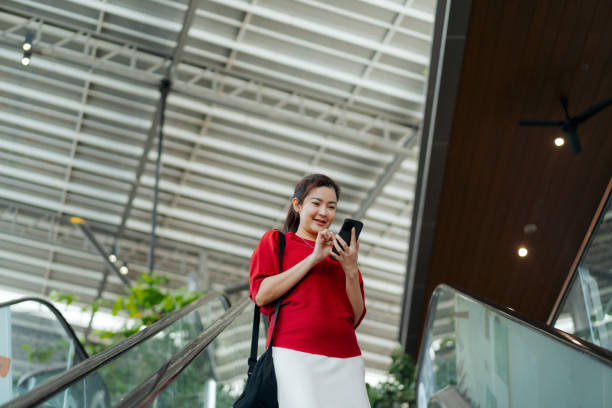 istock woman in a red blouse uses her smartphone to explore AI-powered features while riding an escalator in a modern, bright public space, showcasing a tech-driven lifestyle. 2178110818