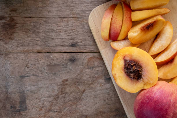 Fresh peaches from the orchard, both whole and sliced for immediate consumption, are on a wooden table. Peaches are a sweet and tangy fruit rich in antioxidants that help nourish the skin, making it smoother, softer, and more hydrated.