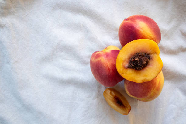 Fresh peaches from the orchard, both whole and sliced for immediate consumption, are on a white plate. Peaches are a sweet and tangy fruit rich in antioxidants that help nourish the skin, making it smoother, softer, and more hydrated.