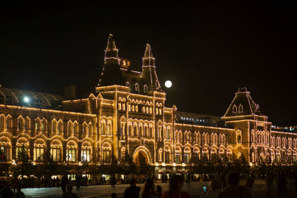 Tverskaya Street is filled with heavy traffic, while the historic Hotel Metropol is brightly illuminated with decorative string lights. The hotel's intricate facade and domed roof are visible, along with festive lighting on nearby trees. A \