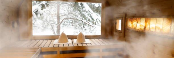 Photograph of the inside of an empty dry sauna with large windows. Walls and benches made of wood and a tile floor.