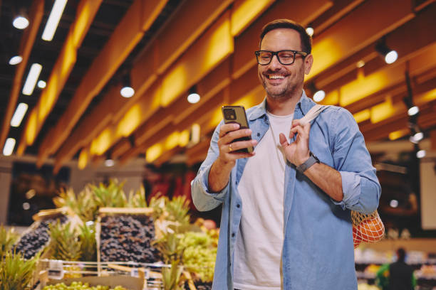 istock Happy man using mobile phone app while buying groceries in supermarket 2178134928