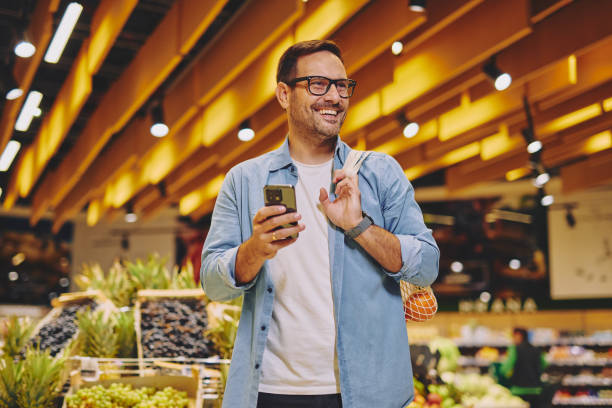 istock Happy man using mobile phone app while buying groceries in supermarket 2178134953