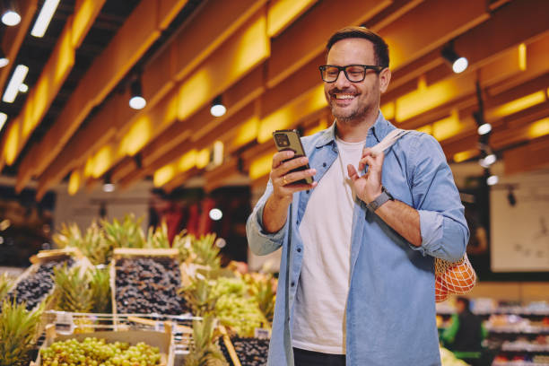 istock Happy man using mobile phone app while buying groceries in supermarket 2178134954