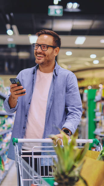 istock Happy man using mobile phone app while buying groceries in supermarket 2178135088