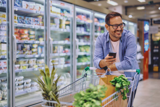 istock Happy man using mobile phone app while buying groceries in supermarket 2178135156