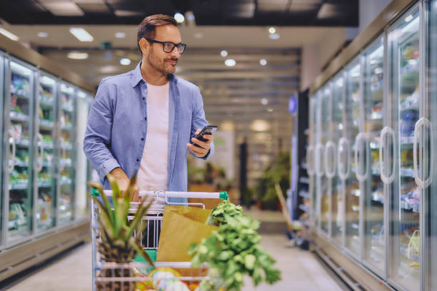 istock Happy man using mobile phone app while buying groceries in supermarket 2178135181