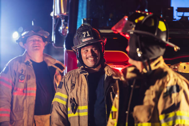 istock Multiracial group of firefighters by firetrucks at night, smiling 2178143662