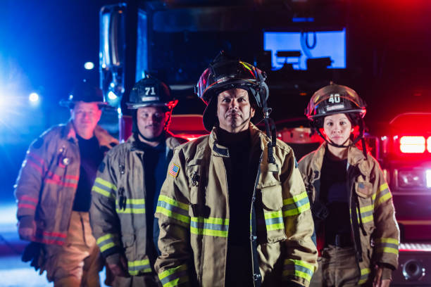 Multiracial group of firefighters by firetrucks at night