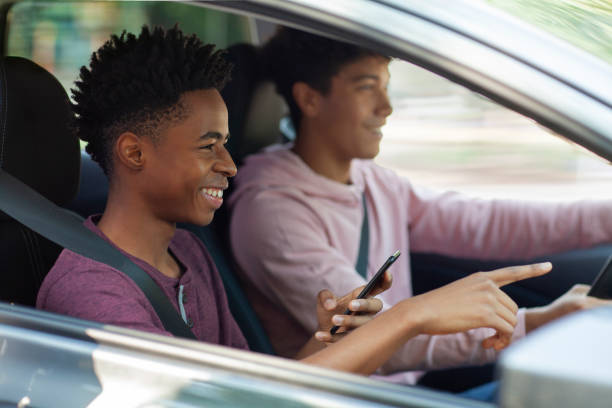 istock Young Black ethnicity teenager boy using sharing smart phone while sitting in car with friend wearing seat belt pointing forward using map 2178144623