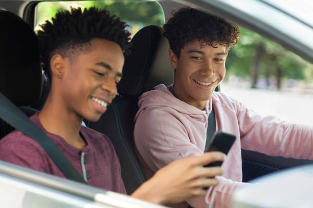 istock Young Black ethnicity teenager boy using sharing smart phone while sitting in car with friend wearing seat belt 2178144630