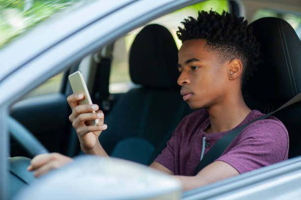 istock Young Black ethnicity teenager boy using looking at smart phone while driving in car wearing seat belt 2178144679