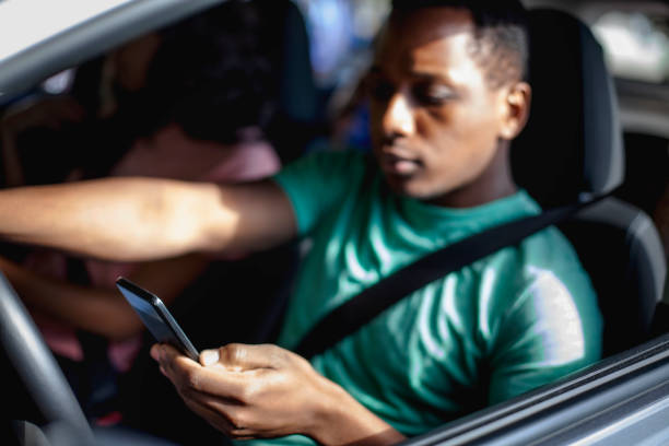 istock Young Black ethnicity teenager boy using looking at smart phone while driving in car wearing seat belt 2178144866