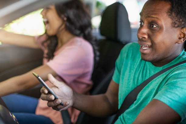 Young Black ethnicity teenager boy using holding smart phone while driving in car wearing seat belt distracted car accident crash