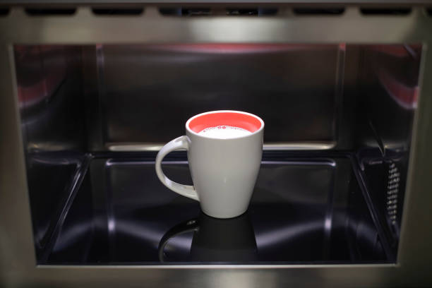 istock heating a white milk cup with a red interior inside a stainless steel microwave, a mug of milk in the kitchen microwave 2178146391