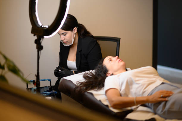 Beautician applying permanent eyebrow makeup on woman