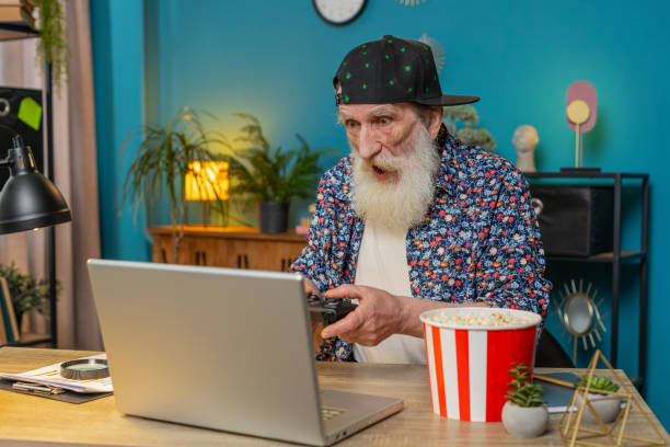 istock Excited happy senior man celebrating victory in play video game on laptop using controller joystick 2178147345