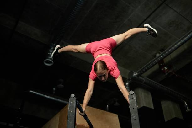 istock Strong Woman Balancing in Handstand on Parallel Bars with Legs Spread in Gym 2178153742