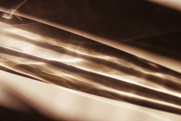 Abstract close-up featuring blurred radial patterns with a strong light source, possibly from a lamp with a ridged surface. The image shows various shades of gray and white with hints of iridescence, suggesting reflections or refracted light. The texture appears glossy, creating a visual rhythm of lines converging towards a bright focal point, lending a dynamic sense of depth and movement.