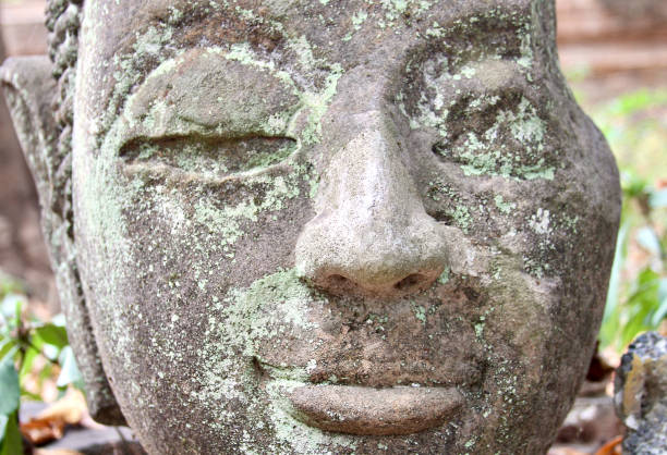 EXCU smiling crumbling stone Buddha face with lichens at Wat Umong in Chaing Mai, Northern Thailand.