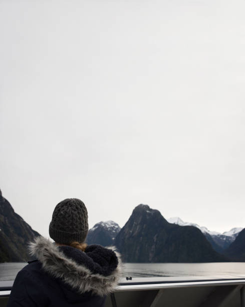 girls in winter clothes watchin the mountains from a boat.