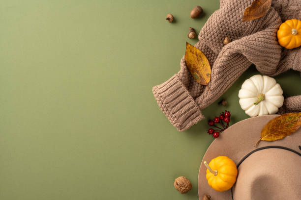 istock Cozy autumn scene featuring a warm sweater, pumpkins, and hat with falling leaves on a green backdrop 2178175922