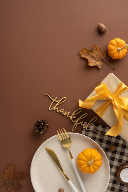 istock Elegant vertical Thanksgiving table setting featuring a plate with cutlery, pumpkins, leaves, and a thank you sign on a brown background 2178175932