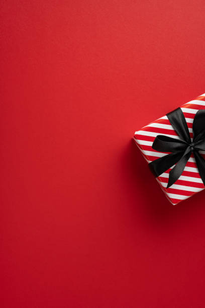 istock A vibrant vertical red background highlights a beautifully wrapped gift box with a black ribbon, ideal for holiday celebrations and Black Friday promotions 2178175960