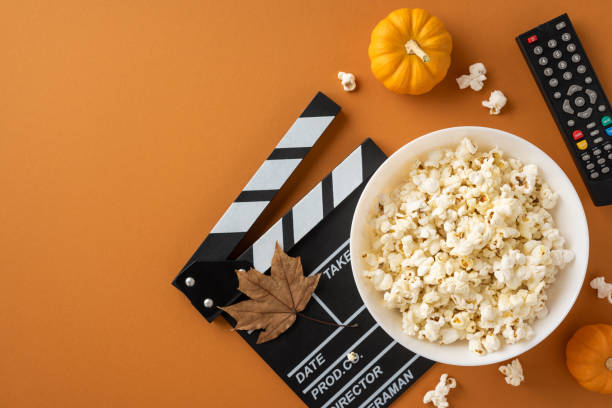 istock A cozy autumn setting featuring a bowl of popcorn, a cinema clapperboard, a pumpkin, and a remote, evoking a movie night atmosphere 2178175963