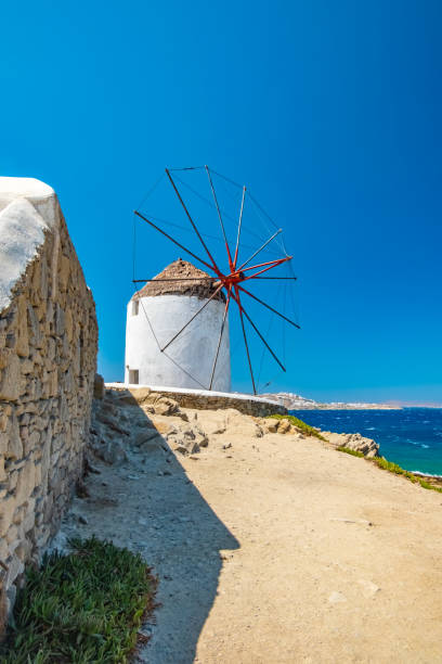 An old traditional whitewashed windmill with a thatched roof on the Greek Island of Mykonos, Greece. Set against a blue cloudy sky and the Aegean Sea.