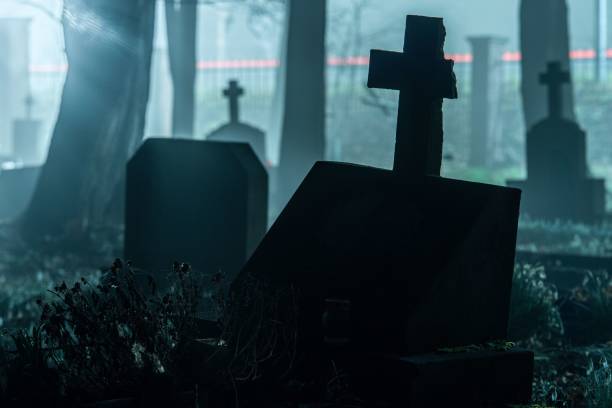 istock Misty cemetery with old gravestones and a cross illuminated by eerie light 2178177687