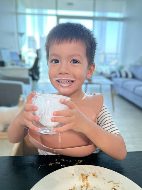 Child smiling while holding a glass with yoghurt drink remnants.
