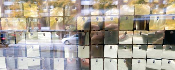 A shimmer wall backdrop made of square sequin panels reflecting the lights and movement of a bustling city street. This close-up photo was taken through a shop window on a busy street in Malmö, Sweden.