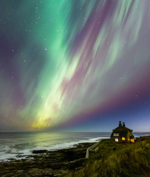 The Northern Lights over a cottage perched on cliffs overlooking the sea on the Northumberland coast during the extreme solar storm of 10th October 2024