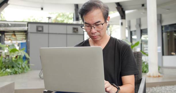 istock Asian businessman Middle-aged working using laptop outdoors. Financial communication business. Senior man wear glasses reading financial graph charts business info computer. Online meeting technology 2178204281