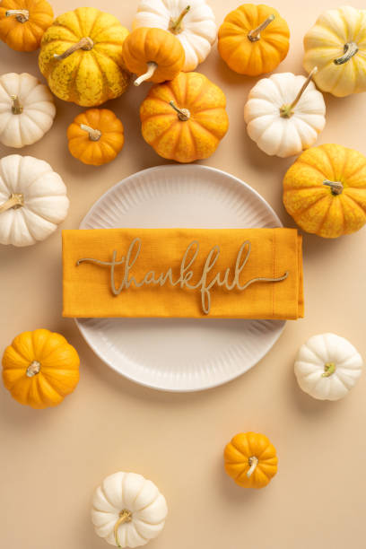 istock Festive vertical Thanksgiving table setting featuring a white plate, orange napkin with thankful text, surrounded by small pumpkins 2178209043