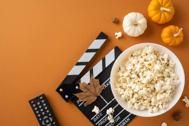 istock A cozy setup for an autumn movie night featuring popcorn, pumpkins, a clapperboard, and a remote on a rustic orange background 2178209044