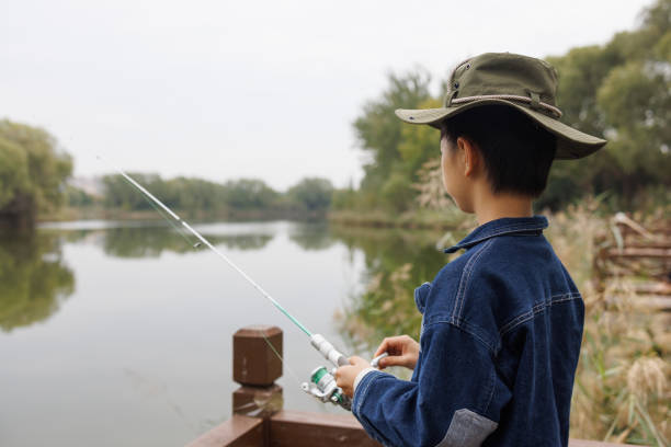 An Asian elementary school student is fishing in a pond
