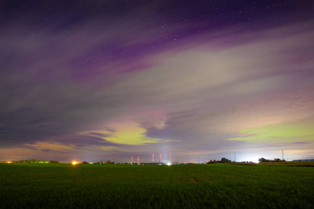 A colorful aurora lights up the sky over a peaceful field, blending vibrant shades with the night’s quiet.