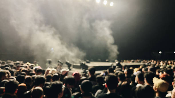 Blurred image of a crowd at concert with stage lights and smoke.