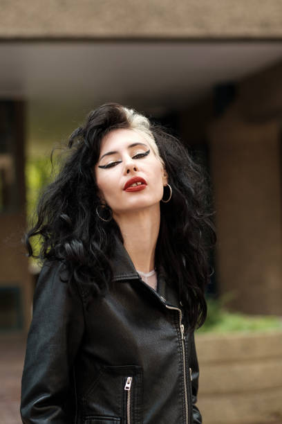 Authentic female rocker posing in front of camera outside. Black leather jacket and big earrings and heavy make-up.