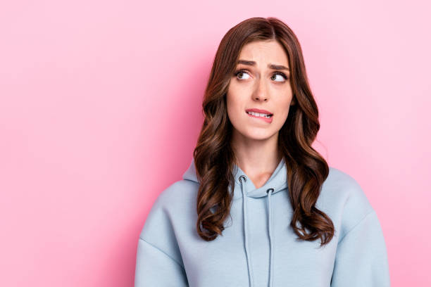 istock Photo of doubtful unsure girl dressed grey sweatshirt biting lip looking empty space isolated pink color background 2178226469