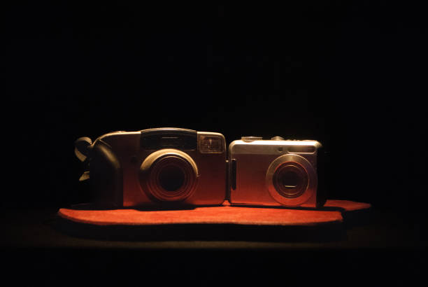 This still-life image captures two vintage film cameras on a wooden surface, illuminated by warm, cinematic lighting. These analog cameras recall a time of manual focus and 35mm film, known for their durable build and the rich, textured images they produced. A perfect display of retro photography gear with a nostalgic ambiance.