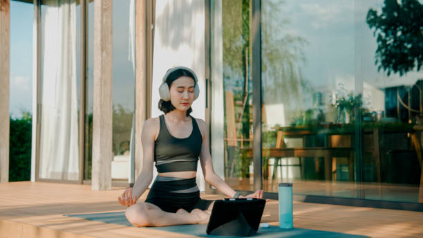 istock Young Asian woman stretching herself following instructions in online class while doing yoga at home. 2178229977