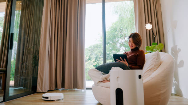 istock Young Asian woman turning on air purifier and vacuum cleaner with smart home functionality while sitting in the living room. 2178234806