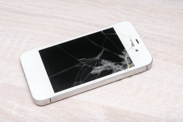 A broken cell phone with a cracked screen on a wooden table. The phone is in pieces, and the screen is shattered. Concept of loss and despair, as the phone is no longer functional