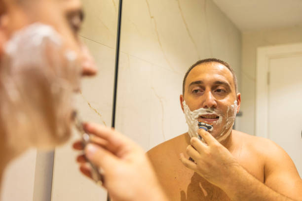 istock Man with shaving foam on his face standing in bathroom, looking at mirror, shaving his face beard. 2178246784