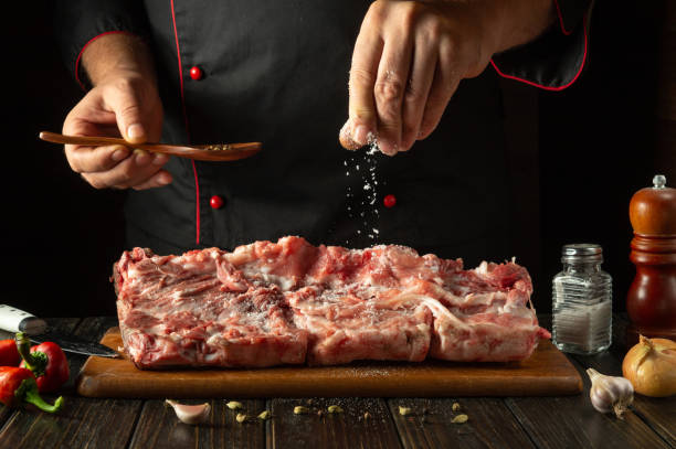 istock Chef sprinkles raw lamb meat with salt. Preparing a large steak of raw meat before roasting. Working environment in a hotel kitchen 2178253156