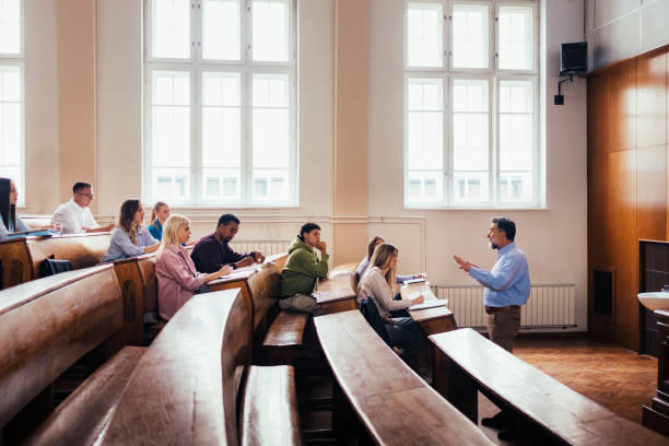 A professor teaches a group of attentive students in a university lecture hall. The classroom setting fosters an engaging educational environment with diverse individuals and learning activities.